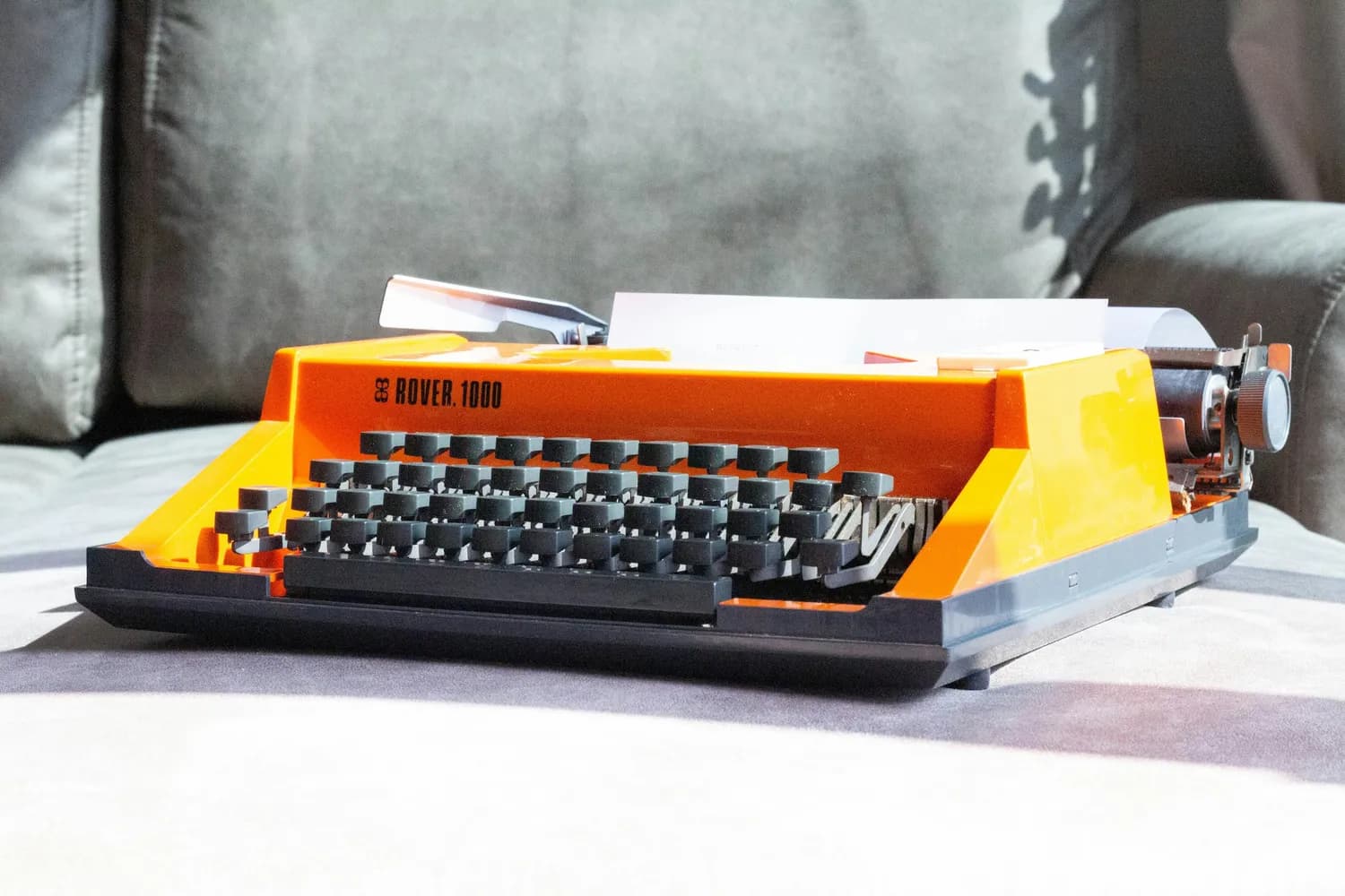 Orange portable typewriter on a grey sofa, seen from the front